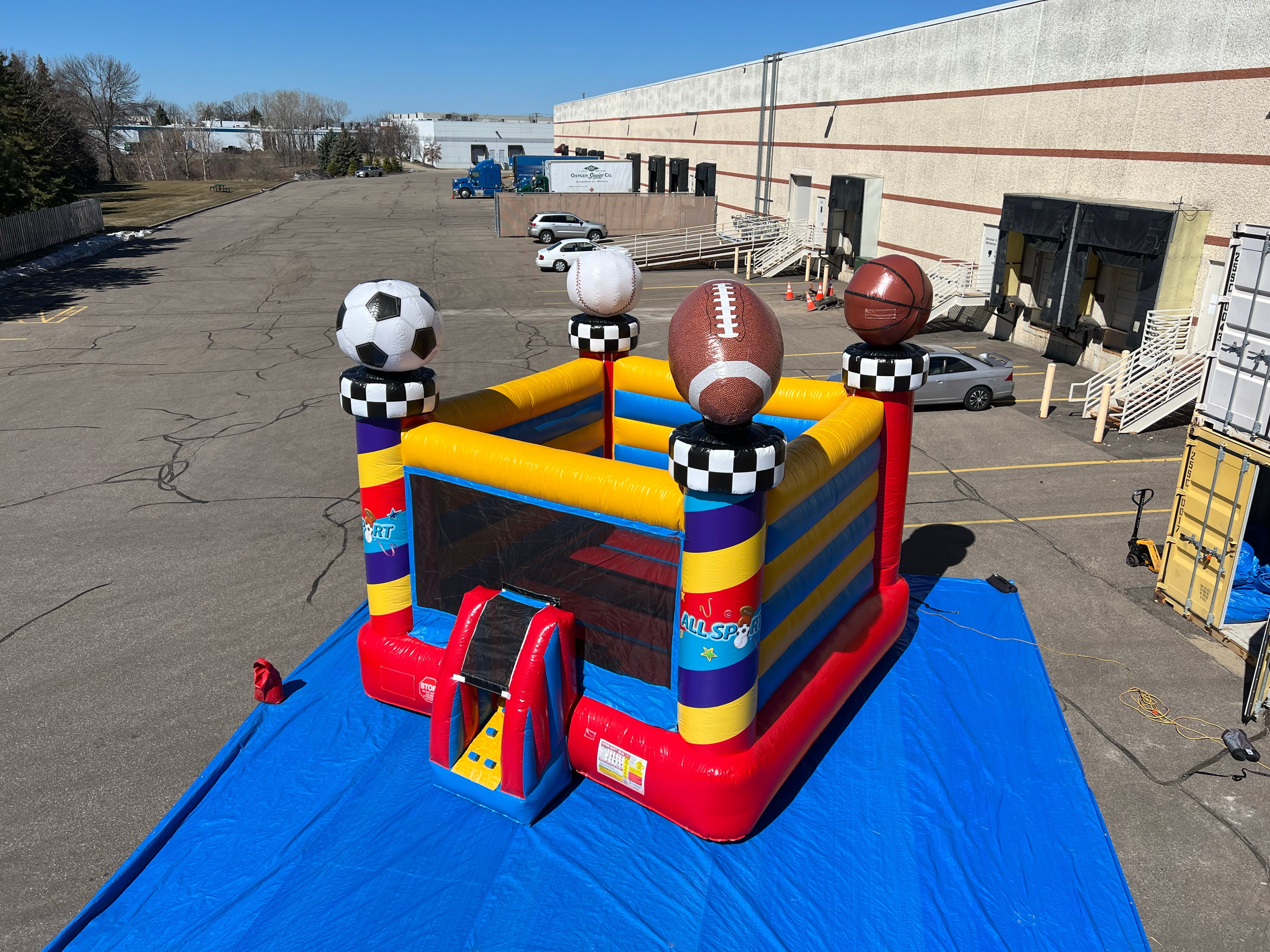 All Sport Bouncer Inflatable with sports ball decorations setup outside on large blue tarp