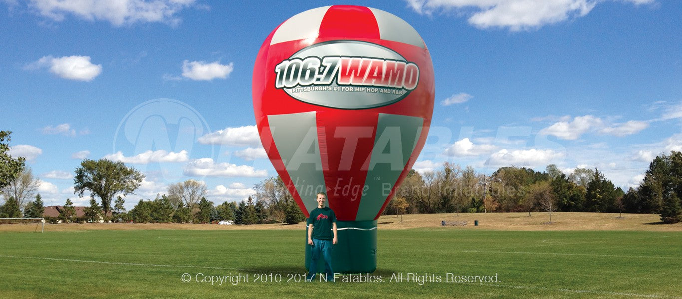 Giant red and silver hot air balloon shaped advertising inflatable with branding set up in a park.  